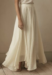 Jupe maxi blanche, avec un tissu texturé, une taille élastique et une silhouette fluide. L'ourlet est asymétrique, avec des panneaux superposés.