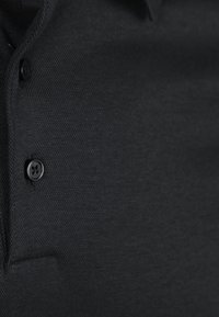 Zwarte poloshirt met een textuurstof, een knoopsluiting en een klassiek kraagontwerp. Het oppervlak heeft een subtiel patroon voor extra detail.