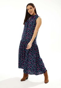 Navy sleeveless dress with a floral pattern featuring pink and teal accents, a button-up collar, and a flowy tiered skirt. Paired with brown boots.