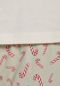 Korte mouw crèmekleurig shirt boven lichtgroene onderdelen, beide met een patroon van rode zuurstokken. Zacht stof met een gladde textuur.