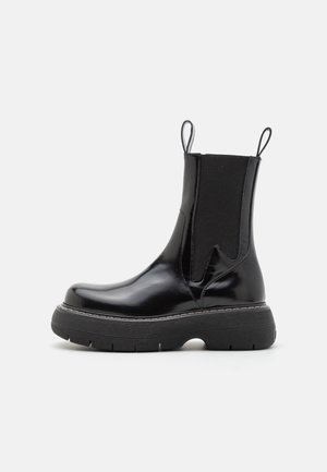 Black leather ankle boot with elastic side panels, rounded toe, and thick rubber sole. Features pull tabs for easy wear.