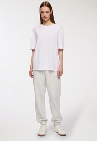 T-shirt bianca oversize, maniche corte, scollatura rotonda, abbinata a pantaloni della tuta grigi chiari, con polsini elastici e sneakers bianche.