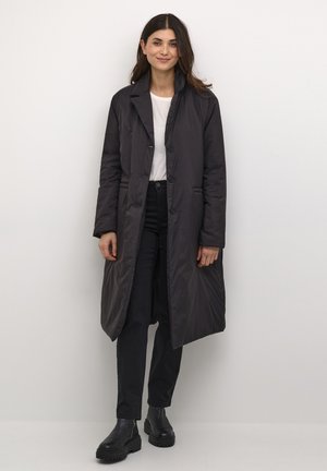Padded dark gray coat with a long silhouette, single-breasted buttons, and side pockets, paired with black pants and boots.