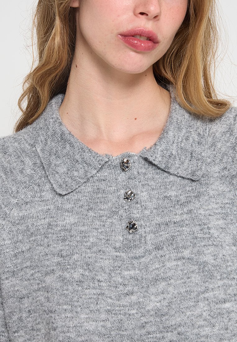 Grijze gebreide trui met een kraag en drie decoratieve knopen. Zachte textuur met een subtiel heatherpatroon.