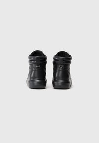 Botas de cuero negro con forma redondeada, cuello acolchado, tira de agarre y suela de goma texturizada. Presenta detalles de costura y un diseño elegante.