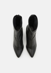 Bottes noires en cuir jusqu'à la cheville avec un bout pointu et des détails de couture subtils. Texture lisse et fermeture éclair à l'arrière.