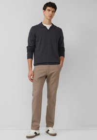 Donkergrijze textuurtrui met V-hals en kraag, gecombineerd met beige broek en witte sneakers met groene accenten.