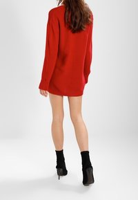 Roter gerippter, übergroßer Pullover mit langen Ärmeln, der einen lässigen Schnitt hat. Getragen mit schwarzen Knöchelsocken und High Heels.