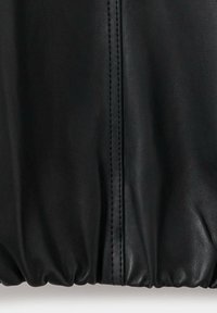 Gros plan sur un tissu en cuir noir avec des coutures verticales et un détail élastique froncé sur le bord inférieur.