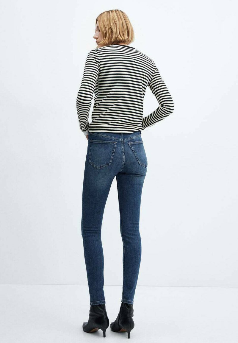 Schwarz-weiß gestreiftes Langarmhemd kombiniert mit dunkelblauen Skinny-Jeans und schwarzen Knöchelboots. Die Jeans verfügen über Gesäßtaschen.