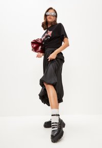 Tricou oversized negru cu litere roșii, fustă din satin neagră cu detalii plisate, pantofi chunky cu platformă neagră, geantă roșie și șosete albe.