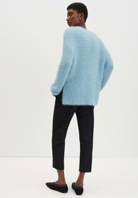 Flauschiger, hellblauer Oversize-Pullover mit abgesenkten Schultern, kombiniert mit schwarzen, kürzeren Hosen und schwarzen Ballerinas, die mit silbernen Nieten verziert sind.