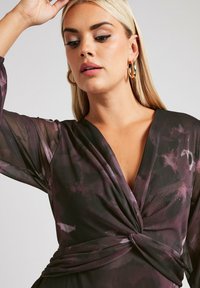 Długa, zwiewna sukienka w czarnej, przezroczystej tkaninie z fioletowymi kwiatowymi wzorami. Posiada długie rękawy oraz skręcone wykończenie w talii. Elegancki dekolt w kształcie litery V.