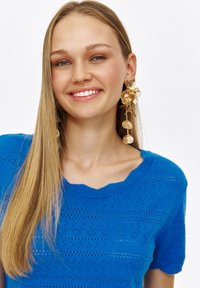 Jasnoniebieski sweter dzianinowy z falbaniastym dekoltem i krótkimi rękawami, o teksturowanym wzorze i lekkiej przezroczystości.