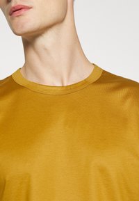 Senapsgul t-shirt med rundad halsringning. Tillverkad av mjukt, slätt tyg med en lätt glans, med korta ärmar och minimala sömmar.