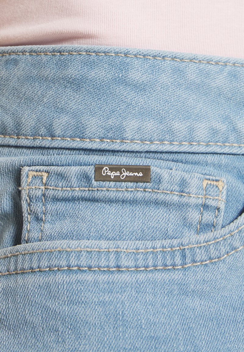 Un jean en denim bleu clair comporte une poche arrière avec une étiquette noire portant l'inscription « Pepe Jeans » brodée en texte cursif blanc.
