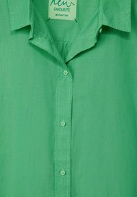 Grönrandig skjorta med mjuk textur, som har en krage, fem knappar och en etikett som läser "ny FAVORIT Street One."