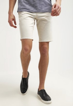 Beige denim short met een aansluitend ontwerp, tot de knie en met een rechte snit. Gecombineerd met zwarte casual sneakers met een geperforeerd patroon.