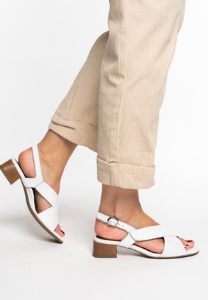 White leather sandals with crossed straps and a low wooden block heel. Detailed with an adjustable buckle for secure fitting.
