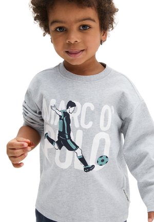 Young child with curly hair wears a gray sweatshirt featuring a soccer player kicking a ball and large white text in the background.