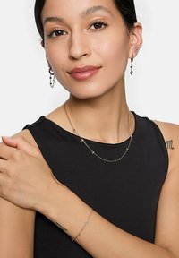 Verfijnd zilverkleurig sieradenset met een halsketting, armband en oorbellen met kleine kraalaccenten, gedragen door een persoon in een zwarte top.