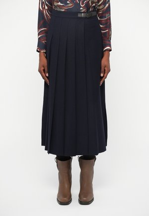 Jupe midi plissée marine avec une ceinture. Fabriquée à partir d'un matériau doux, elle présente des plis verticaux et une texture lisse. Associée à des bottines brunes.