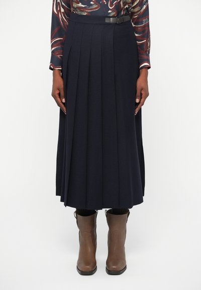 Jupe midi plissée marine avec une ceinture. Fabriquée à partir d'un matériau doux, elle présente des plis verticaux et une texture lisse. Associée à des bottines brunes.