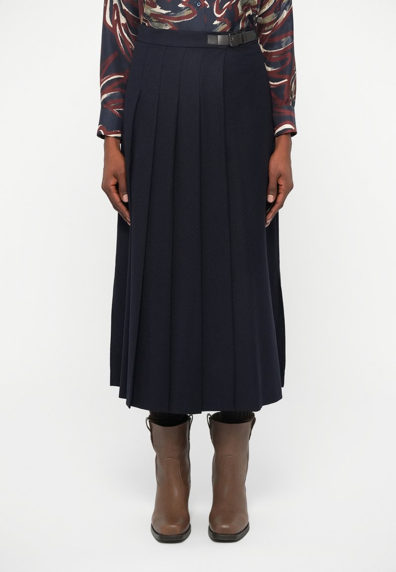 Marinblå plisserad midi-kjol med bälte. Tillverkad av mjukt material, med vertikala veck och en slät textur. Stylad med bruna ankelskots.