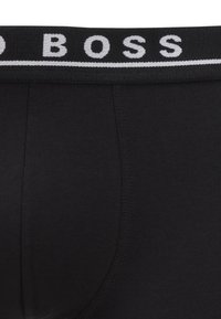 Schwarze Boxer-Shorts mit einem breiten Bund, auf dem der Markenname "BOSS" in kontrastierenden weißen Buchstaben steht. Glattes Baumwollmaterial, figurbetontes Design.