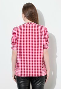 Blouse en vichy rouge et blanc avec manches courtes bouffantes et ourlet droit, associée à un pantalon noir ajusté. Tissu en coton texturé.