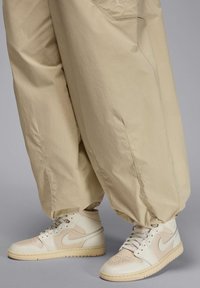 Beżowe, oversize'owe spodnie wykonane z lekkiego materiału, w połączeniu z białymi i kremowymi sneakersami Nike Air Jordan, które mają perforowane noski i logo.