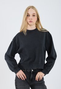 Sweatshirt corto nero con maniche lunghe, realizzato in tessuto morbido. Presenta un colletto rotondo e dettagli di cucitura visibili. Abbinato a jeans scuri.