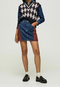 Jeanskörning med en mörkblå och brun färgblockdesign, med hög midja, klassisk sömnad och framfickor. Matchad med en mönstrad stickad väst.