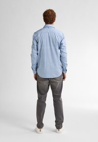 Camicia a maniche lunghe a scacchi blu chiaro con polsini a bottoni, abbinata a pantaloni grigi e scarpe bianche, vista da dietro.