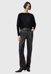 Black oversized sweater with a round neckline paired with high-waisted black leather pants. Texture appears smooth; fitted black boots complete the look.