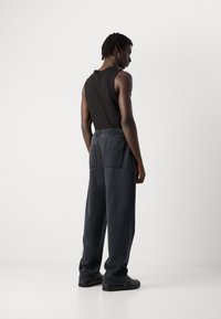 Black tank top paired with loose-fitting dark gray trousers featuring a smocked waistband and two back pockets.