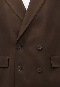 Bruine double-breasted blazer met notch-revers, vier knopen en klepzakken, getoond van borst- tot taillegebied.