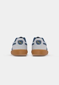 Paire de baskets Puma grises et bleu marine avec semelles en gomme, vues de dos sur un fond blanc.