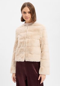 Beige kurz geschnittene Jacke aus Kunstfell mit horizontalen Nähten, rundem Halsausschnitt und langen Ärmeln. Weiche Textur und keine sichtbaren Verschlüsse.