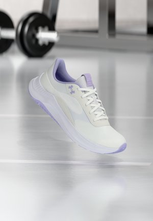 Chaussure de sport blanche et lavande flottant dans une salle de sport avec des haltères flous en arrière-plan, mettant en valeur le design et la semelle de la chaussure.