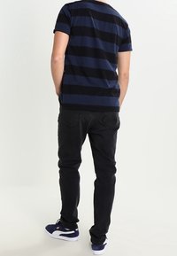 Marineblå og sorte stribede T-shirt med korte ærmer, parret med sorte jeans og mørke sneakers, set fra ryggen. Enkel design, lavet af bomuldsmateriale.