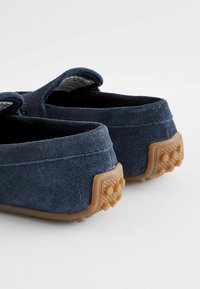 Mocassini in suede blu navy con suola in gomma caratterizzata da dettagli di trazione circolari. Tessuto morbido, senza hardware visibile, design ergonomico.