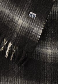 Sciarpa di lana a quadri in nero e grigio con bordi sfrangiati; presenta un piccolo etichetta in metallo argentato con il testo "Tommy Jeans".