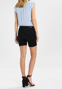 Vaaleansininen pilkullinen pusero lyhyillä hihoilla, yhdistetty mustiin farkkushortseihin ja mustiin korkokenkiin. Sileät materiaalit, rento tyyli.