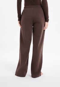 Brązowe spodnie o szerokich nogawkach wykonane z miękkiego materiału z elastycznym pasem w talii. Projekt charakteryzuje się gładką fakturą bez widocznych logo czy wzorów.