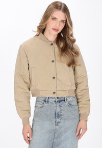 Beige cropped quiltet jakke med en rund krave, knaplukning foran og ribbede manchetter. Glat tekstur, subtil bølget mønsterdetalje.