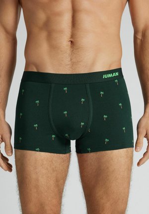 Mandlig torso iført mørkegrønne boxershorts med små palmetræsprints og en mærket taljebånd.