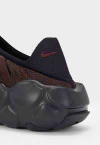 Black and maroon sneaker with a textured knit upper, a distinctive pointed heel, and a chunky, flexible black sole featuring round bumps.