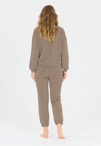 Bruine sweatshirt en bijpassende joggers gemaakt van zachte stof. De sweatshirt heeft lange mouwen en een geribbelde zoom; de joggers hebben elastische boorden.