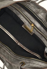 Interno di una borsa in pelle grigia con più scomparti in tessuto nero e zip dorate. Presenta un'etichetta del marchio e dettagli in cucitura marrone.